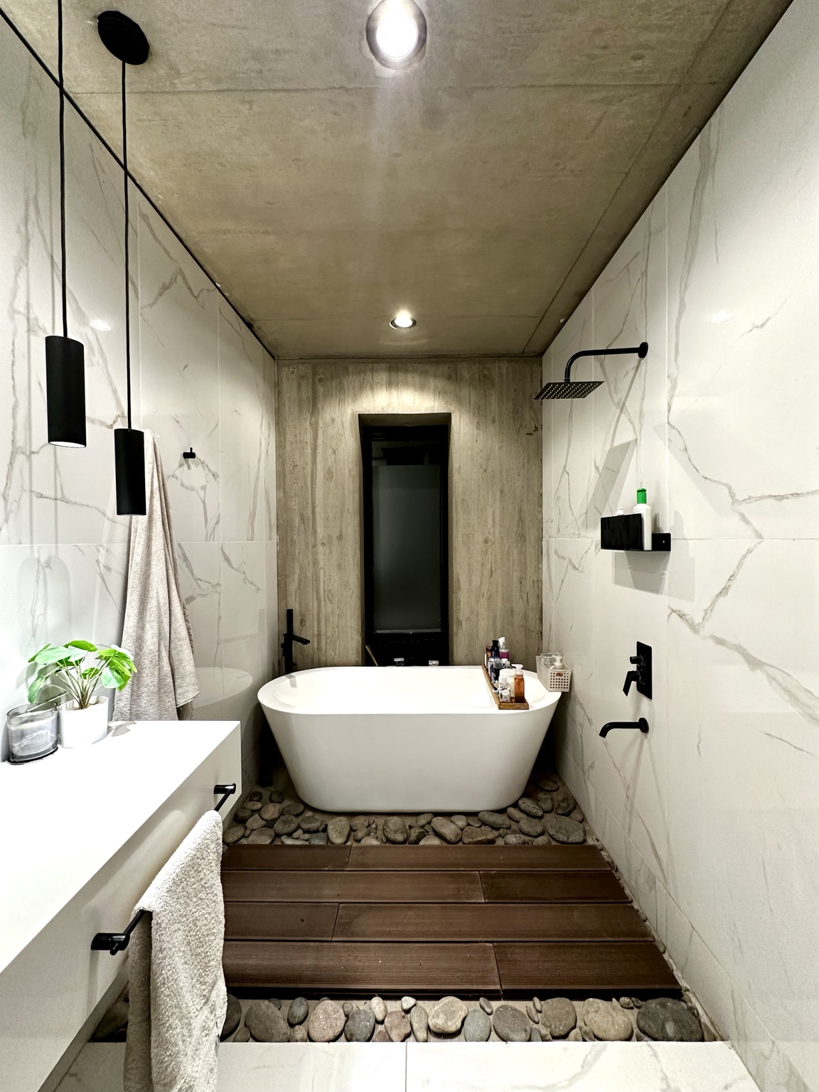 Baño de Casa SI-25 con hormigón visto, revestimiento claro y piso de madera y piedra