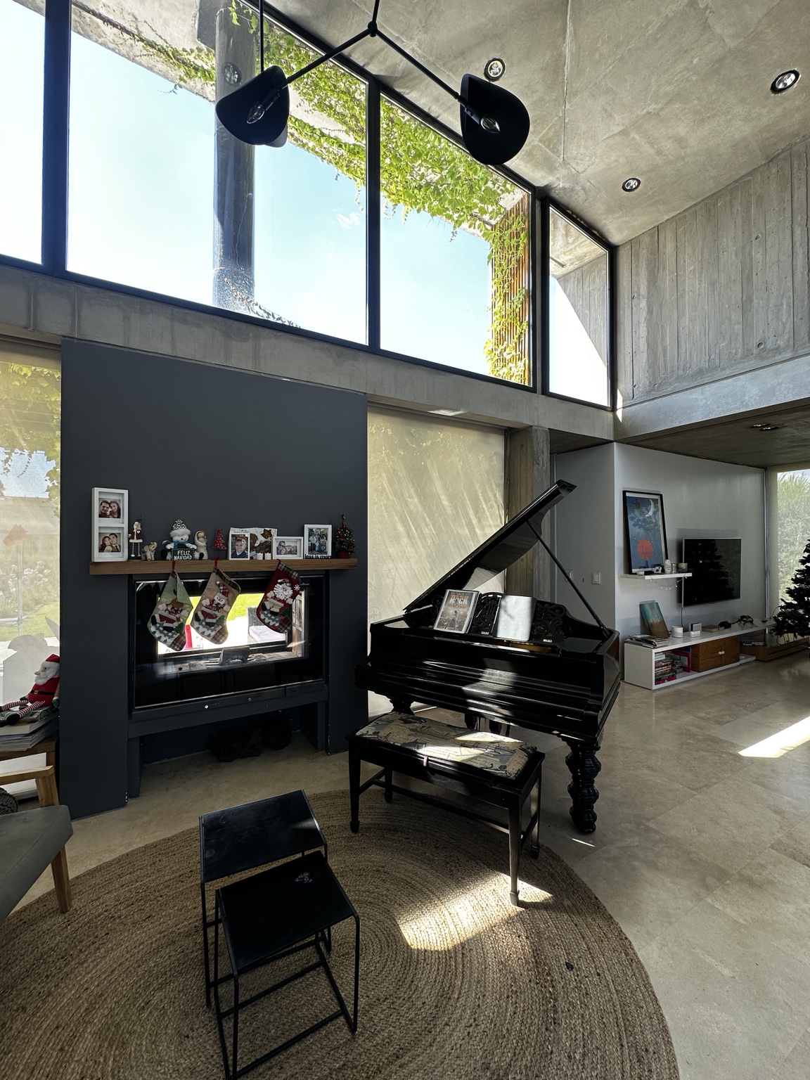 Estar de doble altura de Casa SI-25 con hormigón visto, vegetación y piano